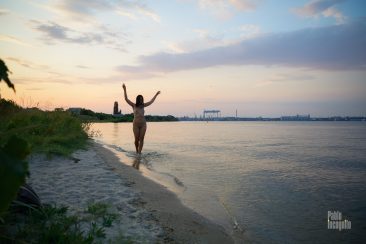 A naked girl walks along the water's edge with her hands up