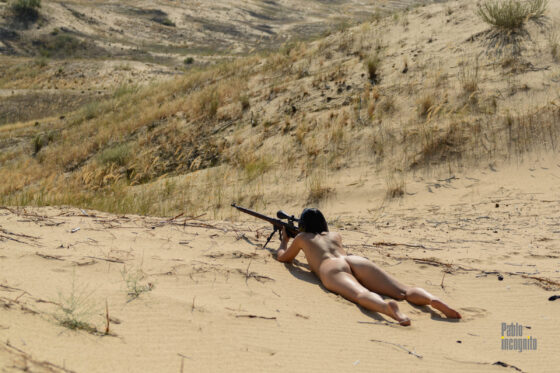 Naked girl sniper shoots from a rifle in the desert