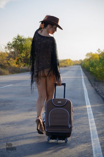 Half-naked girl walks along the road with a suitcase