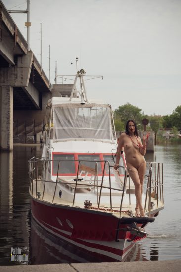 Naked brunette stands on the bow of the boat