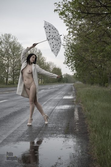 Naked in a raincoat with an umbrella on the road