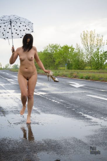 Naked girl splashes through the puddles with an umbrella in her hands