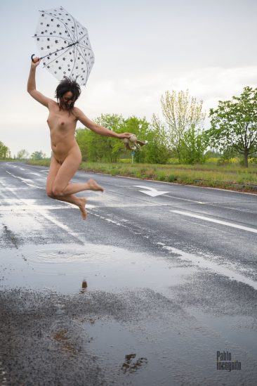 Naked girl jumping barefoot in a puddle in the rain