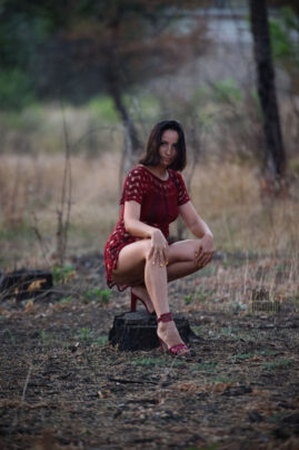 Girl in a short red dress posing on a tree stump in the forest