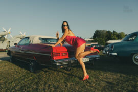 A girl in a crimson dress poses near a crimson Chevrolet Impala. Nude photo by Pablo Incognito