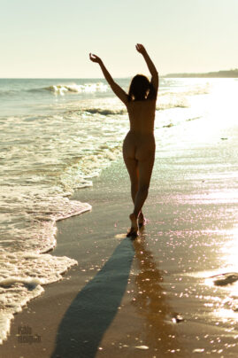 Naked woman walks alone on a wild beach at sunset