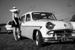 Lady in a hat posing topless near a retro car at an exhibition. Nude photo by Pablo Incognito