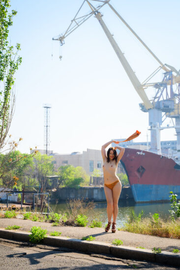 Topless on the background of ship cranes, nude