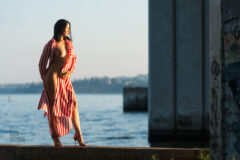 Nude model Iren Adler poses in a striped dress under a bridge by the river. Photo by Pablo Incognito