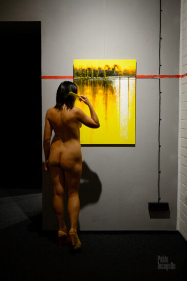 A nude model combing her hair near a painting at an exhibition. Pablo Incognito
