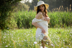 A girl in a short dress and a hat bared her breasts in a field with flowers, nude photo
