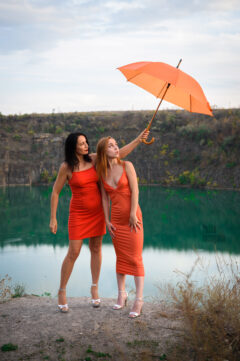 Photo session by the lake. Two girls in orange dresses with an umbrella