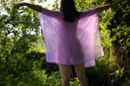 A naked girl in a transparent cape stands with her back