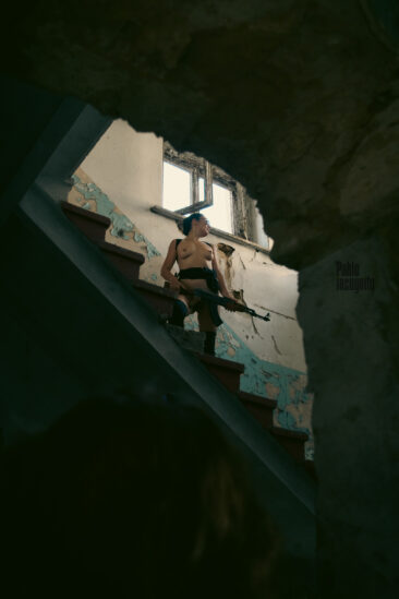 Naked with a machine gun on the steps in the ruins